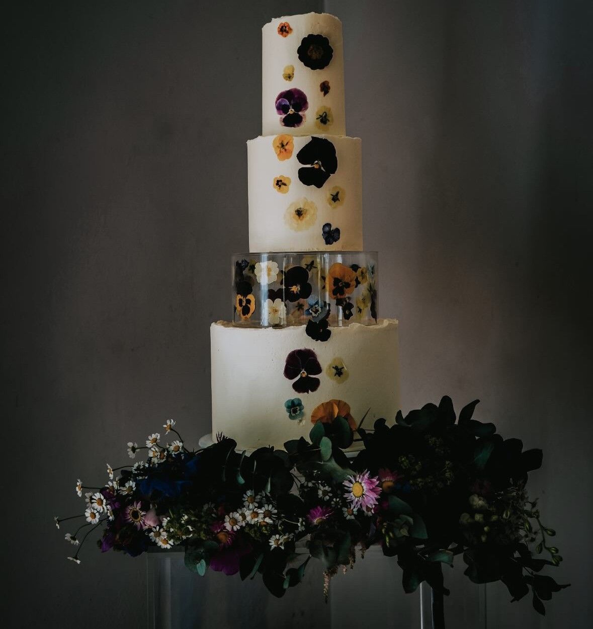 Four-tier white buttercream wedding cake with pressed edible flowers and a suspended floral tier