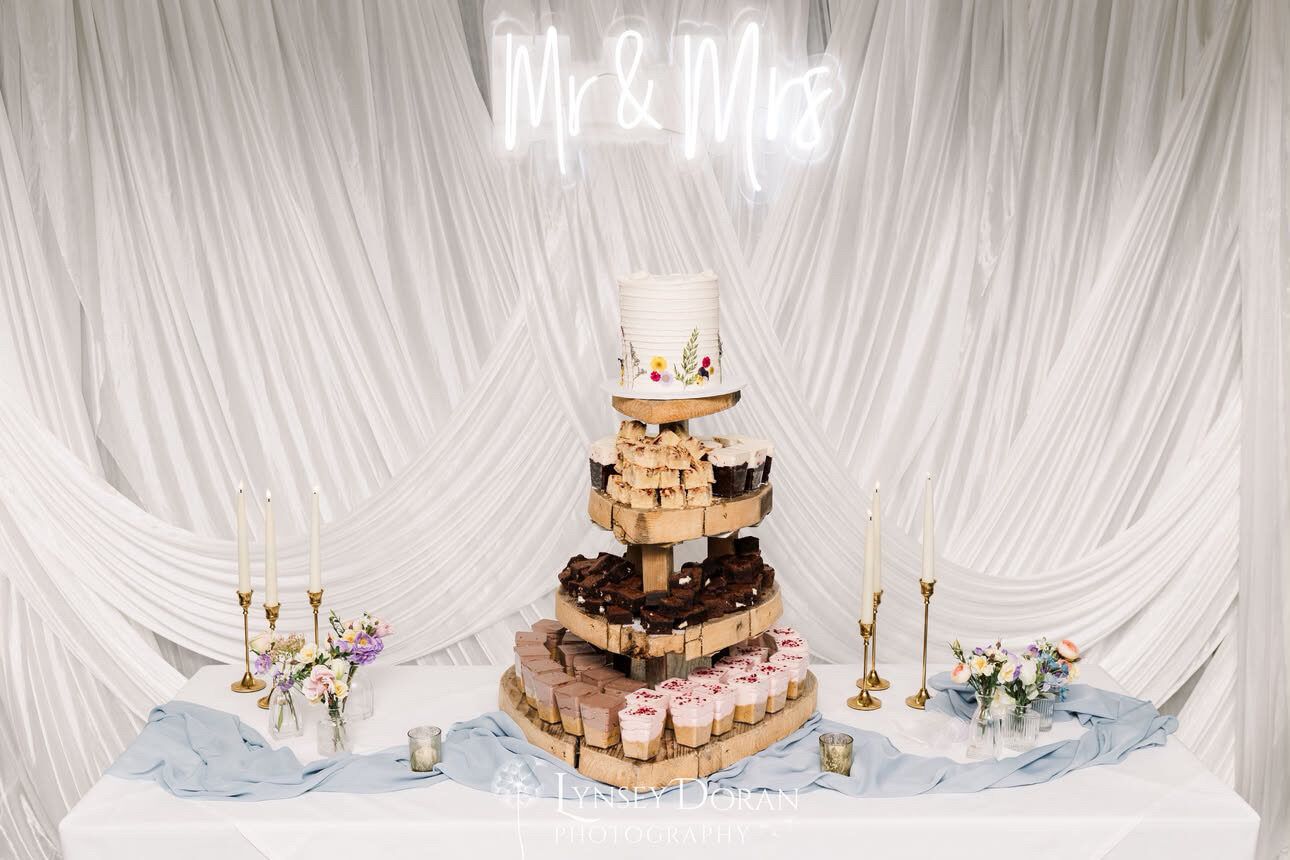 Draped wedding dessert table display with a cutting cake and treats beneath a Mr & Mrs sign