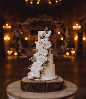 Four tier white wedding cake with a cascade of white orchids on a wooden slice