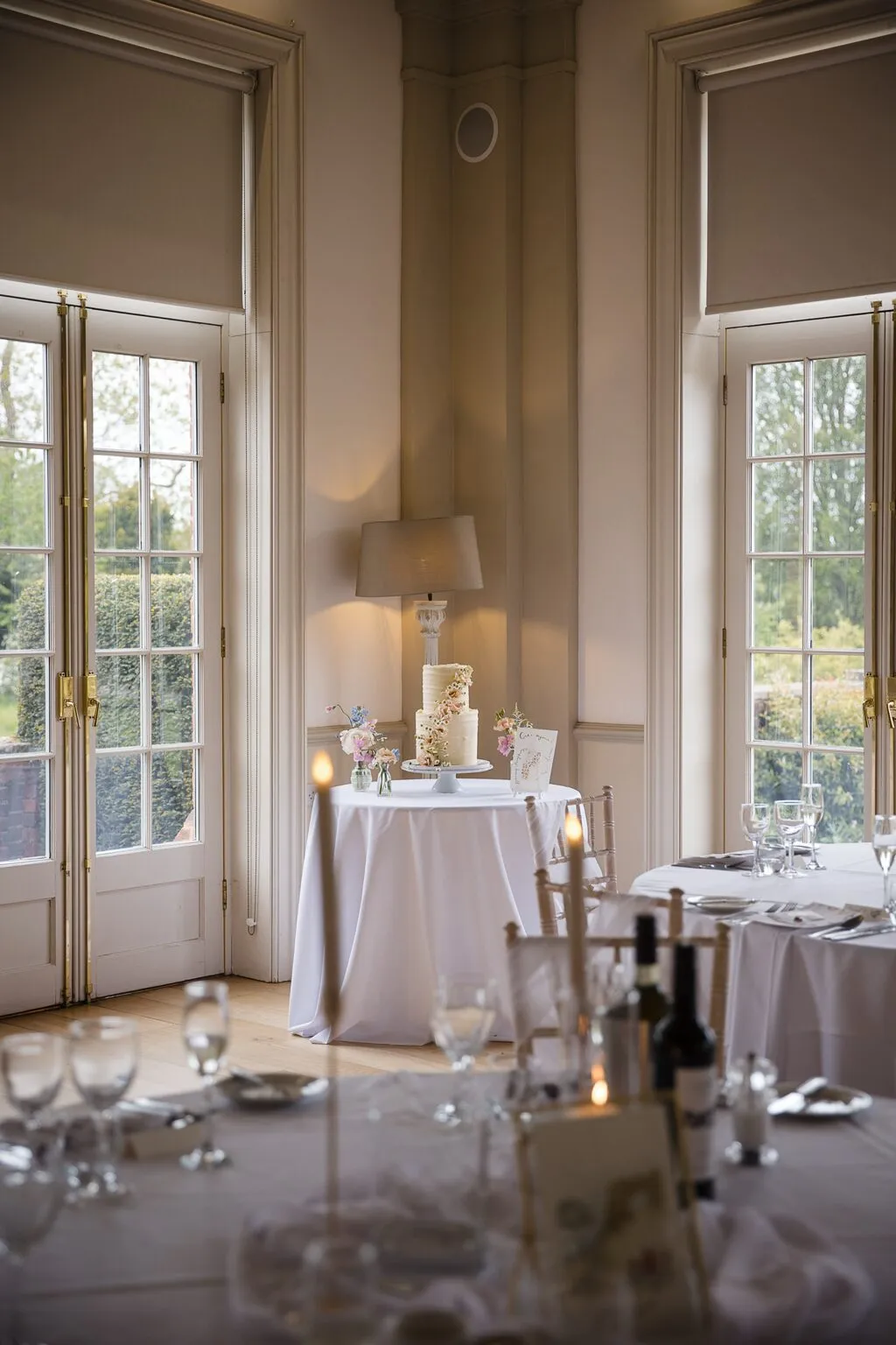 The floral cascade wedding cake on a dressed table beside the windows in the dining room at Hodsock Priory