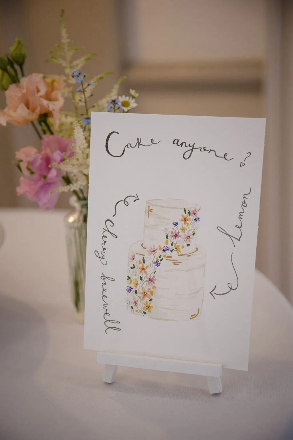 Charlotte’s hand-painted ‘Cake anyone?’ menu illustration beside spring flowers at Hodsock Priory