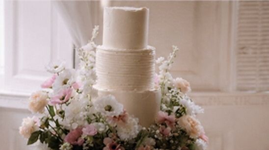 Tall three tier textured white wedding cake surrounded by pink and white flowers