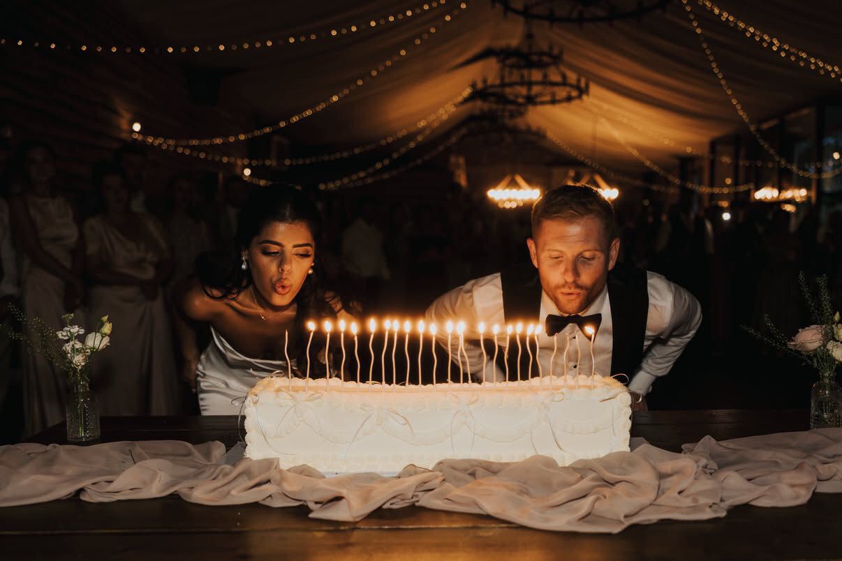Bride and groom blowing out a row of candles on a long Lambeth-piped wedding cake