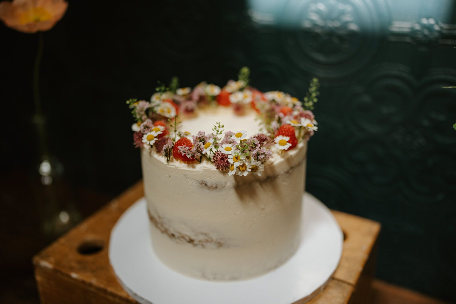 Single tier semi-naked buttercream wedding cake crowned with wildflowers and strawberries